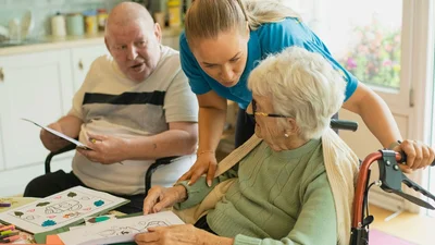 Caregiver assisting an elderly couple with a coloring activity