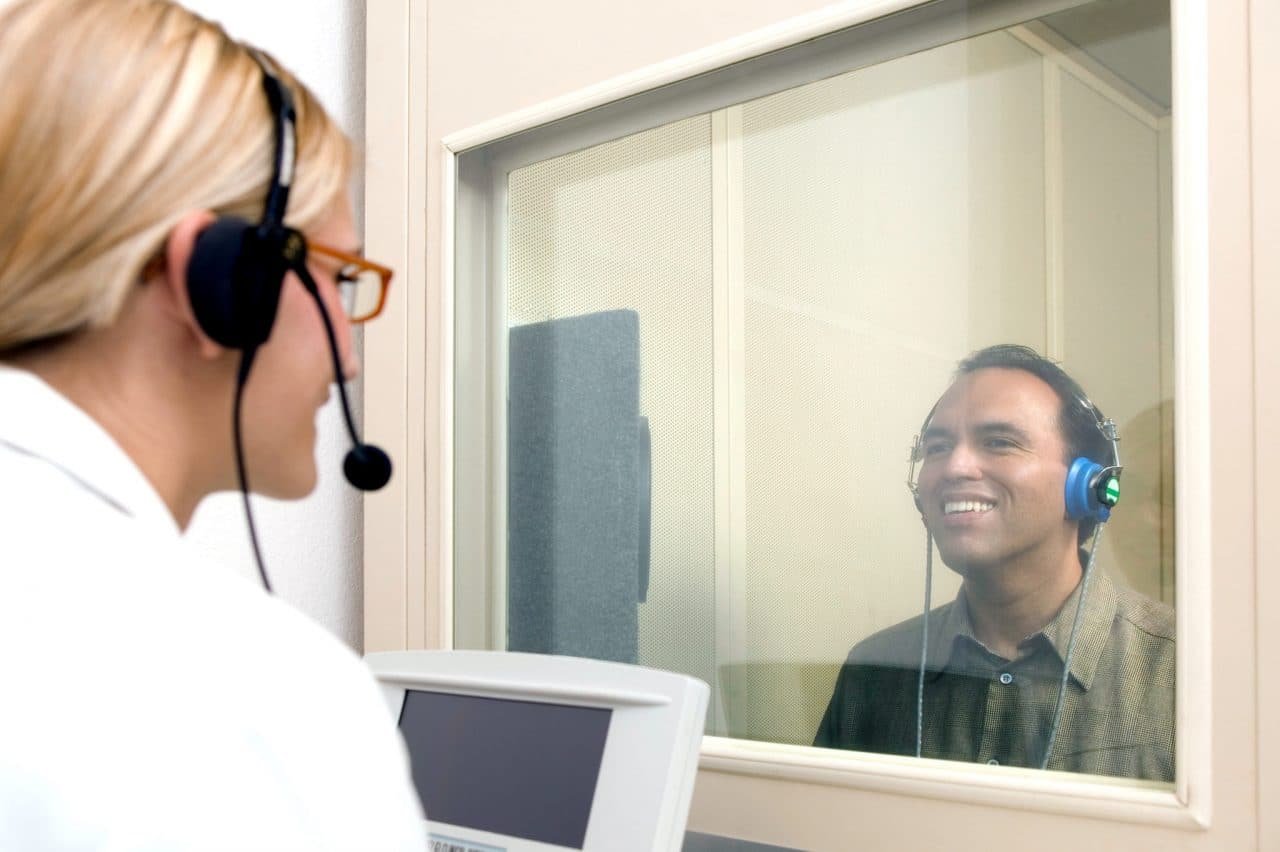Hearing care provider speaking with a patient through the window of a sound-treated test booth