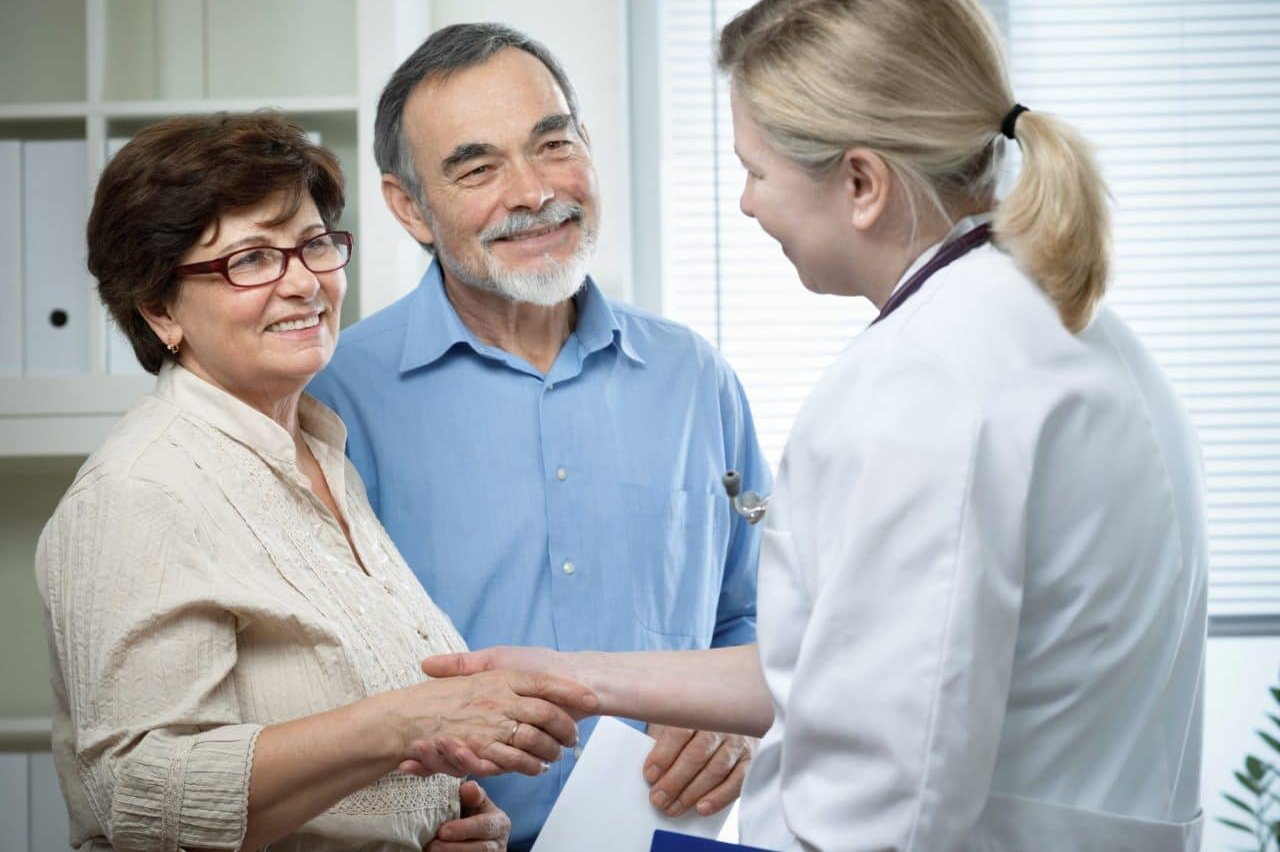 A care provider greeting a smiling senior couple at a hearing appointment