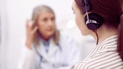 Patient wearing audiometric headphones during a hearing test, with a provider in the background
