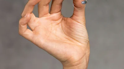 A hand holding a behind-the-ear hearing aid with a thin tube and earmold