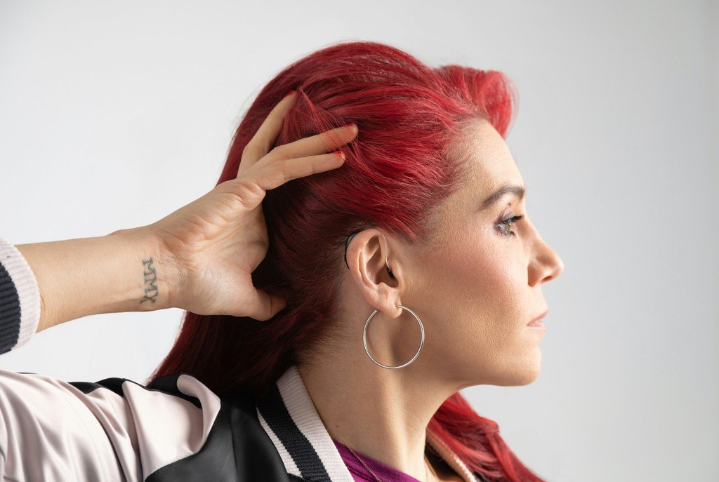 Close-up profile of a woman with red hair pulling her hair back to reveal a behind-the-ear hearing aid