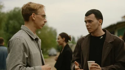 Two men having a conversation outdoors, one holding a drink
